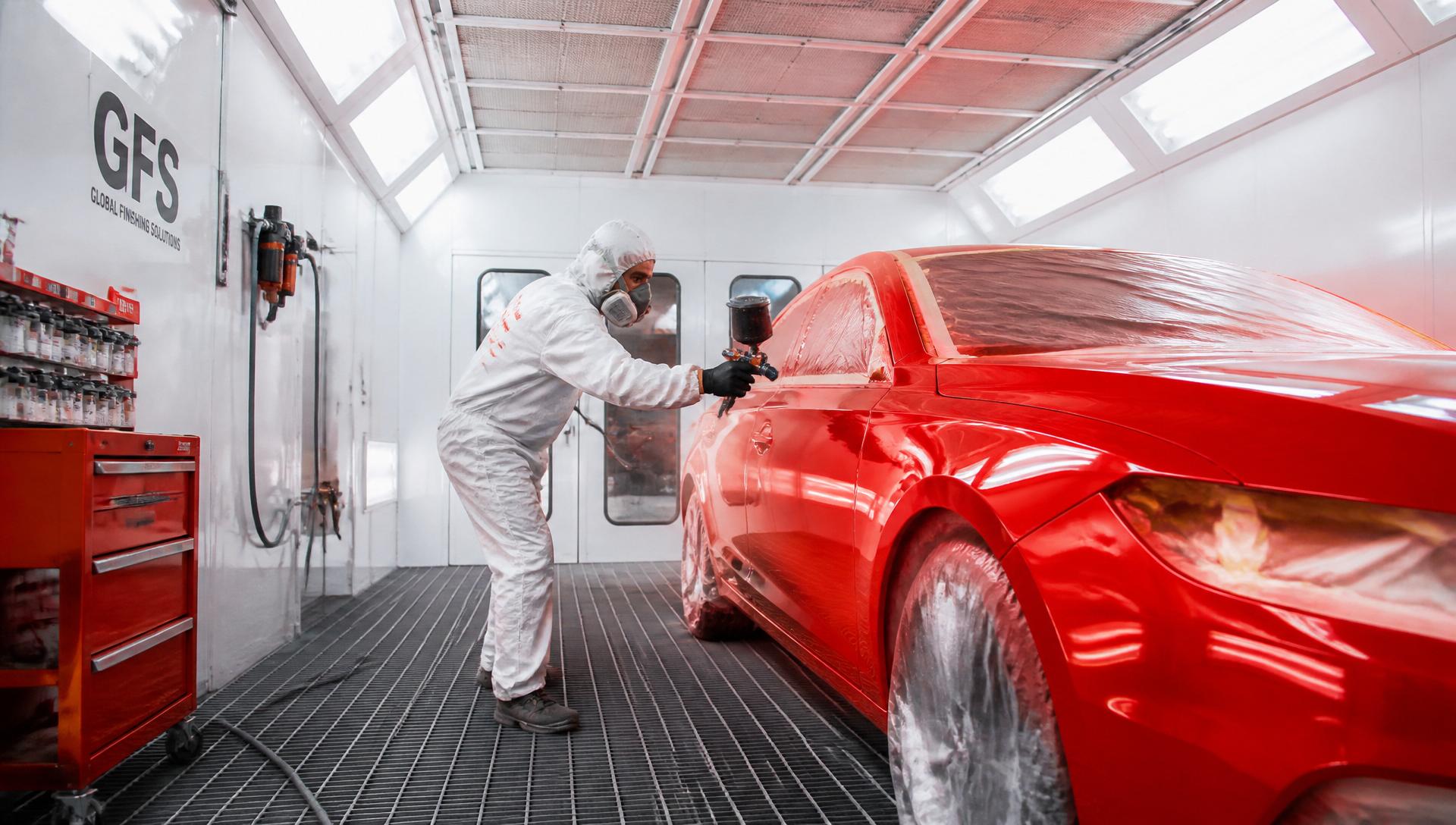 Técnico aplicando pintura automotriz en cabina presurizada profesional